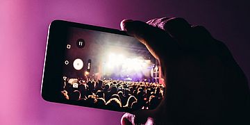 Eine Person filmt ein Konzert mit einem Mobiltelefon.